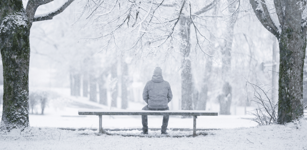 A person sitting alone on a bench in the snow.