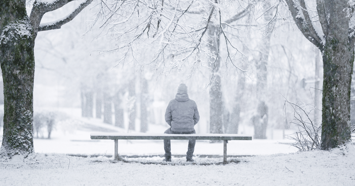 A person sitting alone on a bench in the snow.