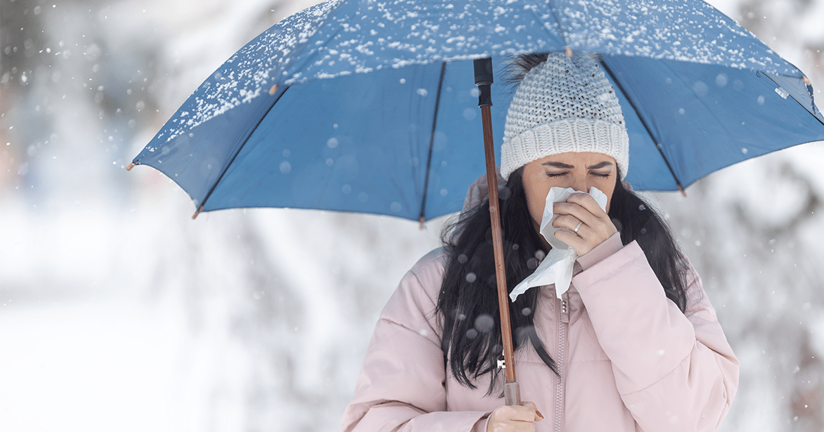 A woman holding an umbrella and blowing her nose.