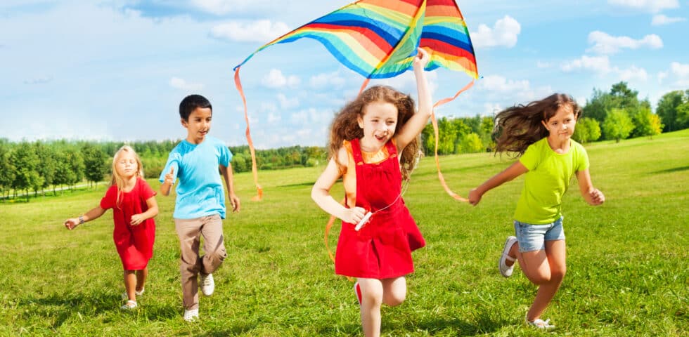 Group Of Four Kids Running In The Park With Kite
