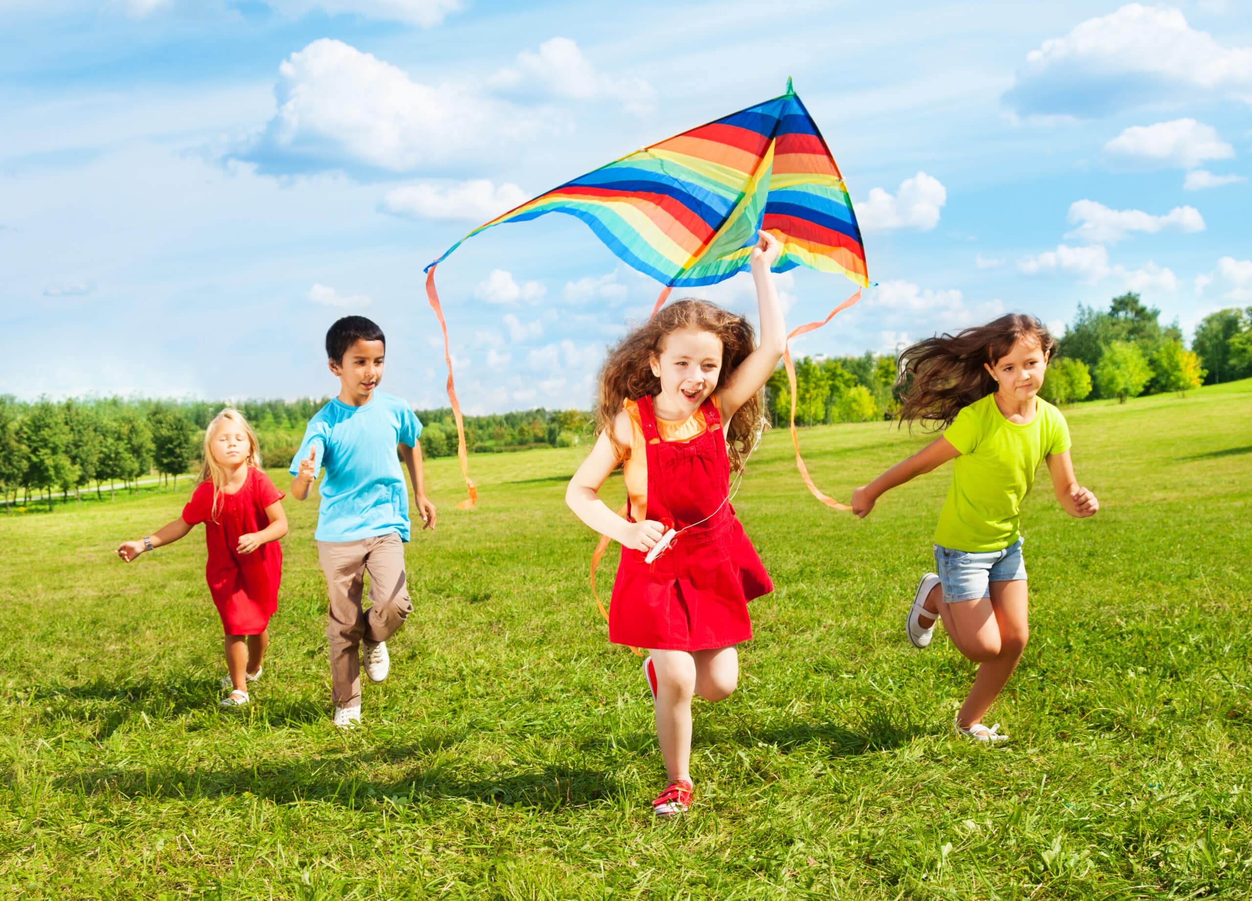 Group Of Four Kids Running In The Park With Kite